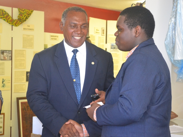 Premier of Nevis Hon. Vance Amory presenting Rol-J Williams with a monetary token from the Board of Directors and staff of the Nevis Historical and Conservation Society at their office on August 05, 2015, before travelling to Vermont in the USA to represent St. Kitts and Nevis at the 2015 Youth Ambassadors Program