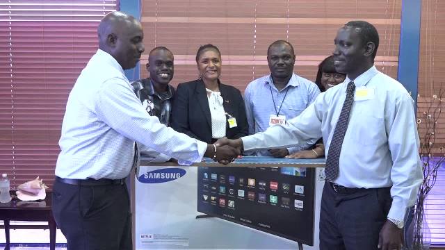 (Right) Mr. Oscar Walters, General Manager for S.L. Horfords (Nevis Center) presents two Samsung 43 inch television sets to Mr. John Hanley, Acting Permanent Secretary in the Ministry of Tourism recently for use at the Vance W. Amory International Airport. Looking on are (l-r) Dawson Ottley, Tourism Officer in the Ministry of Tourism, Ms. Shelagh James, Communications Officer in the Ministry of Tourism, Mr. Daron Sutton, Manager of the Vance W. Amory International Airport and Mrs. Collette Weeks, Protocol Officer at the airport