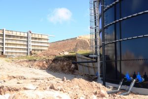A section of the brand new 400,000 gallon steel glass fused water tank at the Hamilton Reservoir on February 19, 2020, stands in the foreground of the fiberglass tank whose function it will replace. The old tank will be demolished and a new filtration system will be erected in its place