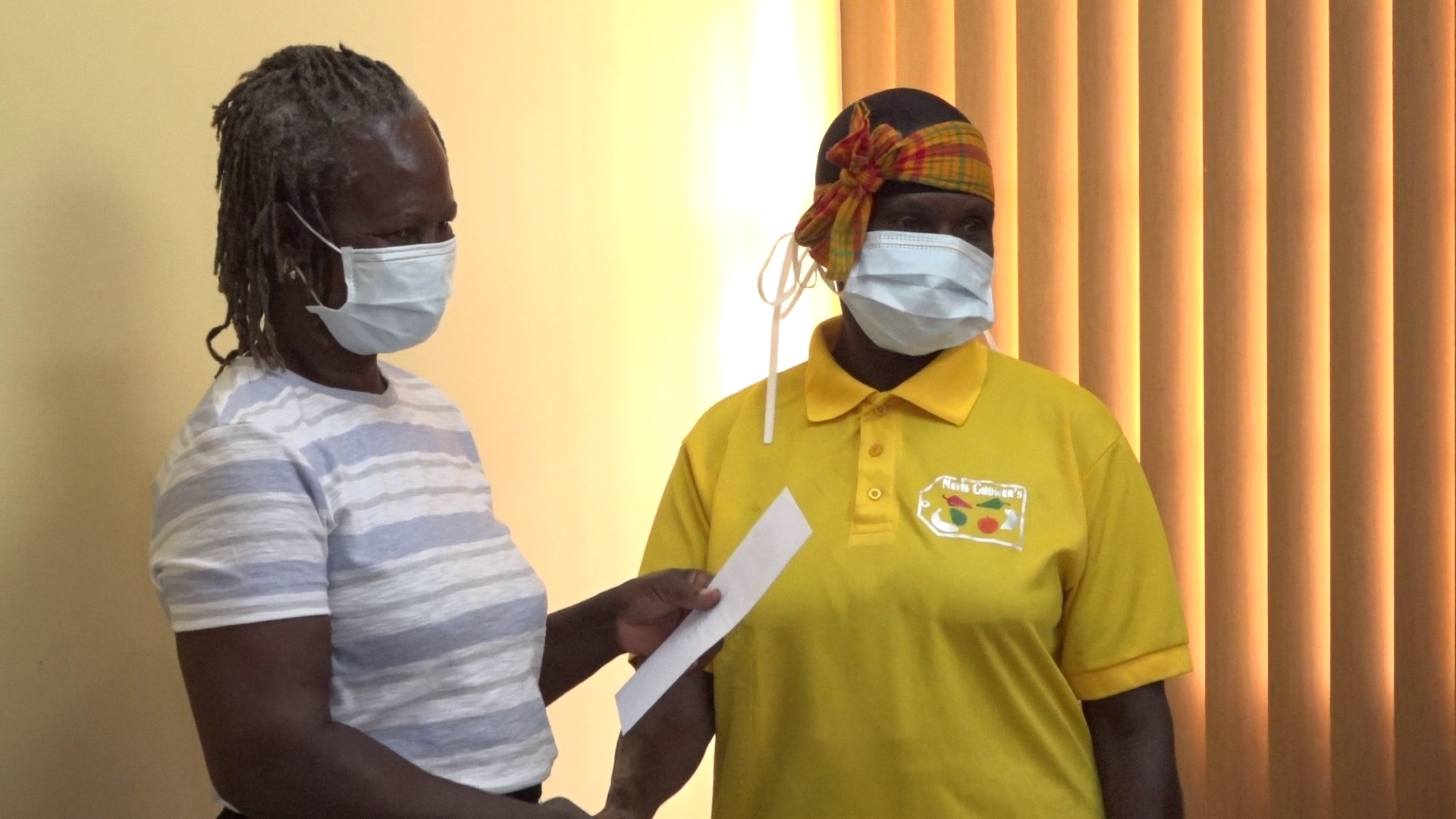 Mrs. Emontine Thompson, President of Nevis Growers Association (right), with recipient Lydia Dore, one of 13 members of the farmers cooperative hands over a monetary donation from the Nevis Growers Association on August 13, 2020, at the Ministry of Agriculture Conference Room at Prospect