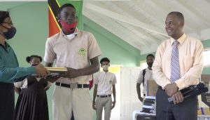 Fifth form student Lebron Senior accepting school supplies from Mrs. Lineth Williams, Principal of the Gingerland Secondary School n October 09, 2020, while Hon. Eric Evelyn Minister of Youth and Community Development in the Nevis Island Administration, and area representative for St. George’s, Gingerland who donated the supplies looks on