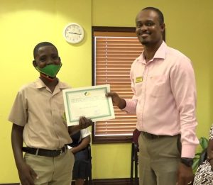Mr. Benjamin Clarke of the Gingerland Secondary School receiving the Bank of Nevis Limited’s Right Excellent Dr. Sir Simeon Daniel Scholarships for 2020 presented by Pheon Jones, Marketing Officer and Member of the Scholarship Committee on December 04, 2020