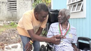 Mr. Nathan “Neville” Sutton, 100, of Rawlins in Gingerland wearing his medal of honour presented to him by Hon. Eric Evelyn Minister of Social Development on Nevis on behalf of His Excellency Sir Tapley Seaton, Governor General of St. Kitts and Nevis shares a light moment with a close friend moment after he received it in celebration of Centenarians Day on May 31, 2021