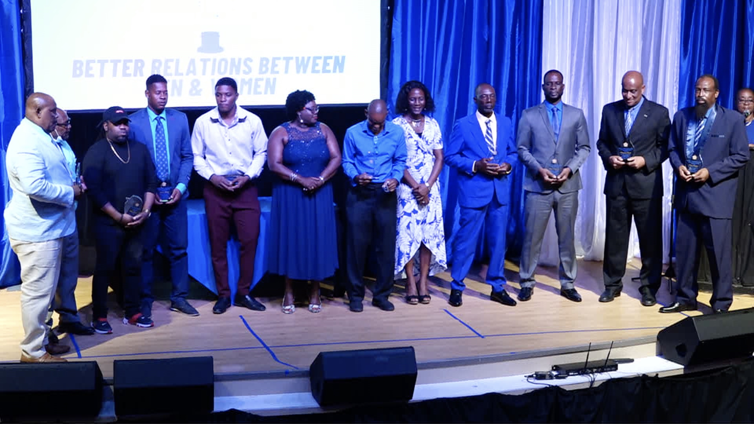 Awardees at the Department of Gender Affairs’ Men’s Day Awards Ceremony (l-r) Mr. Sylvester Pemberton; Mr. Shefton Liburd; Mr. Kareem “LL” Herbert; Mr. Dulani Phillip; Terron Lawrence, son and representative of Mr. Euclid Lawrence; Gareth “Gary” Wade; Ms. Shelisa Martin-Clarke, Permanent Secretary in the Ministry of Health and Gender Affairs; Mr. Alexis Browne; Mr. Leroy Parris Jr; Mr. Masefield Nisbett and Mr. Conrad Smithen with Hon. Hazel Brandy-Williams, Junior Minister of Health and Gender Affairs (sixth from left); and Ms. Shelisa Martin-Clarke, Permanent Secretary in the Ministry of Health and Gender Affairs (fifth from right) at the Nevis Performing Arts Ceremony on November 30, 2021